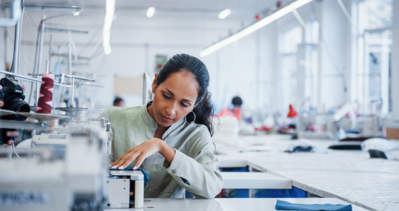 Dressmaker woman sews clothes on sewing machine in factory.